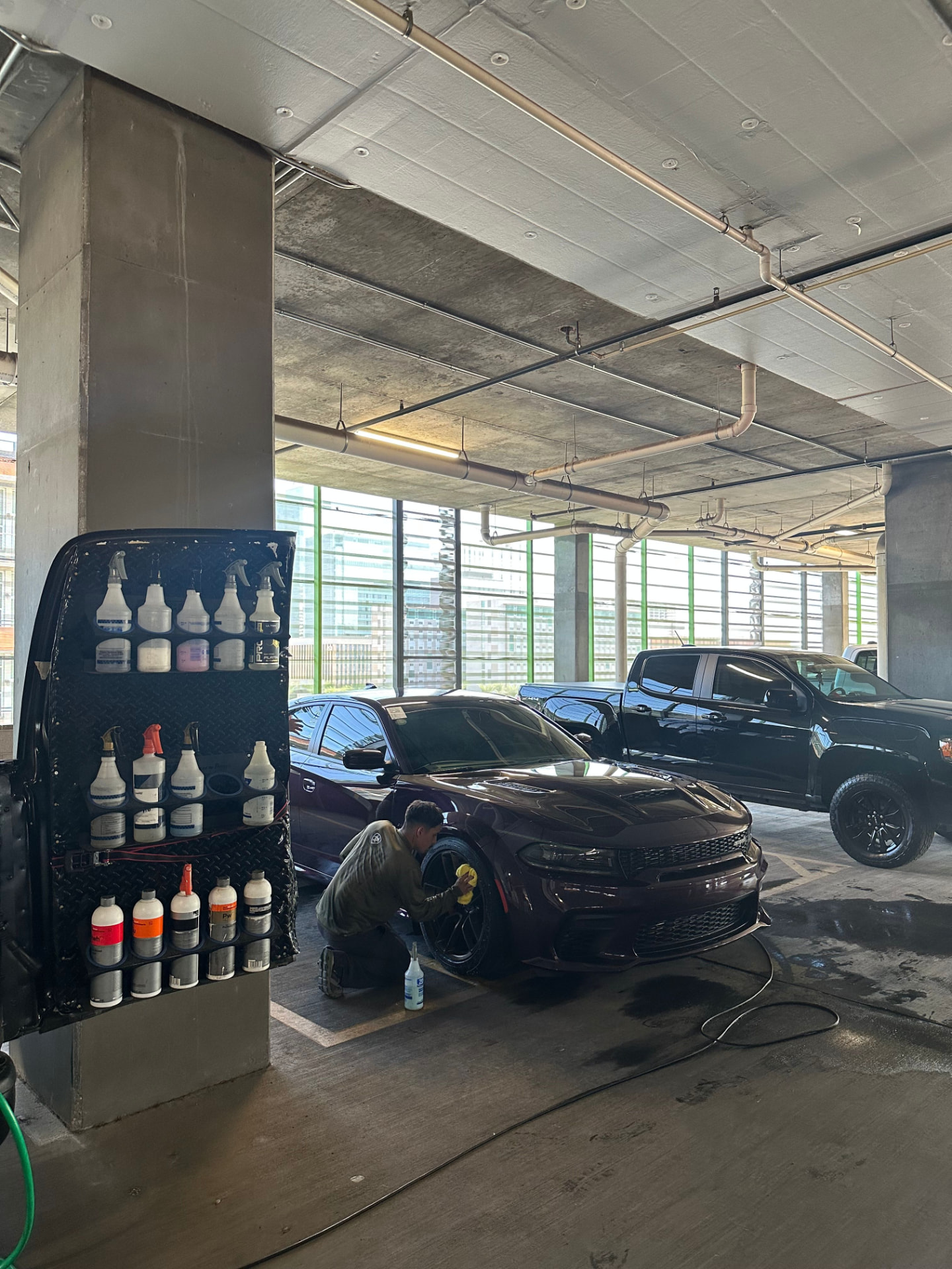 Master Mobile Detailing technician detailing a wheel on a dark Dodge Charger in a Phoenix parking garage with the mobile product rack alongside